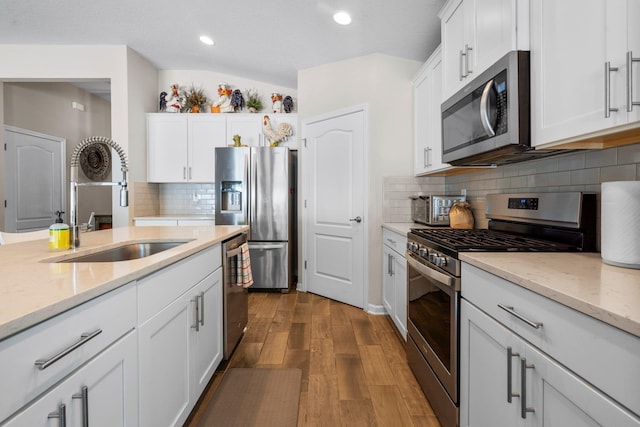 kitchen featuring stainless steel appliances, sink, wood-type flooring, white cabinetry, and lofted ceiling