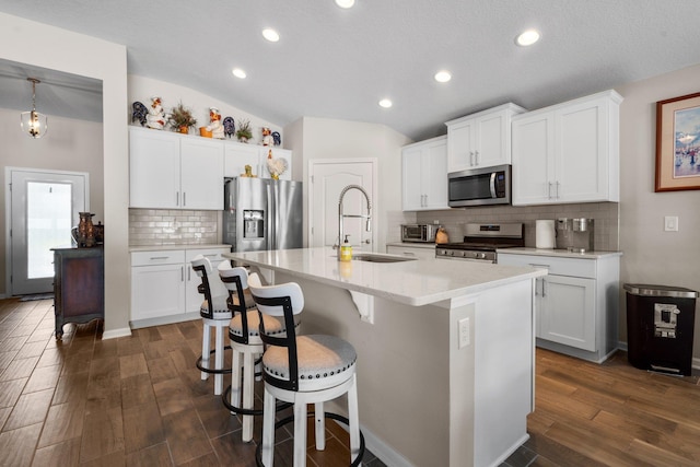 kitchen with appliances with stainless steel finishes, a kitchen island with sink, dark hardwood / wood-style floors, white cabinetry, and lofted ceiling