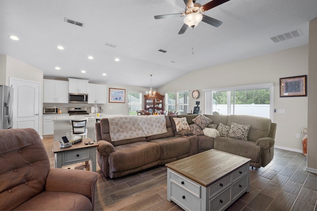 living room with ceiling fan with notable chandelier, dark hardwood / wood-style floors, and vaulted ceiling