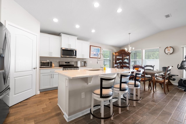 kitchen featuring stainless steel appliances, sink, white cabinets, hanging light fixtures, and an island with sink