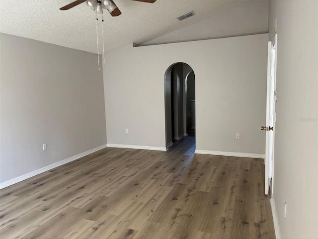 empty room featuring visible vents, a ceiling fan, wood finished floors, arched walkways, and vaulted ceiling