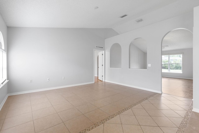 unfurnished room featuring visible vents, baseboards, vaulted ceiling, light tile patterned floors, and arched walkways