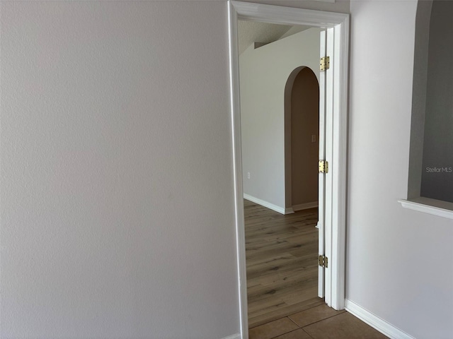 hall with dark tile patterned floors, baseboards, and arched walkways