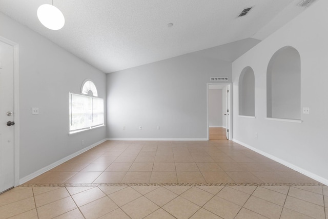 empty room with visible vents, light tile patterned flooring, and vaulted ceiling