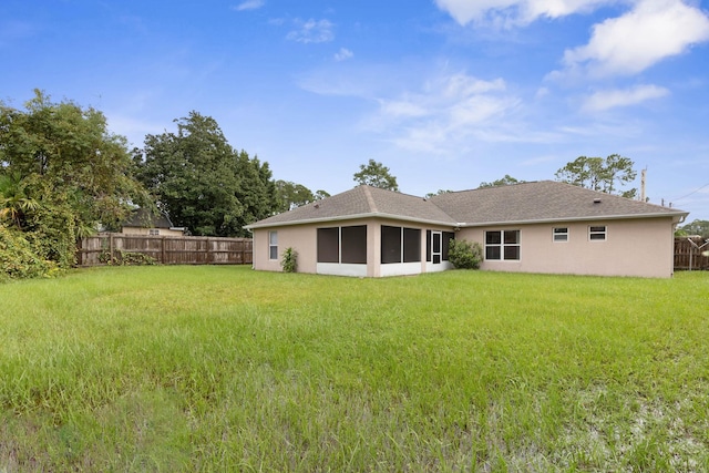 rear view of property featuring fence, a lawn, a sunroom, and stucco siding