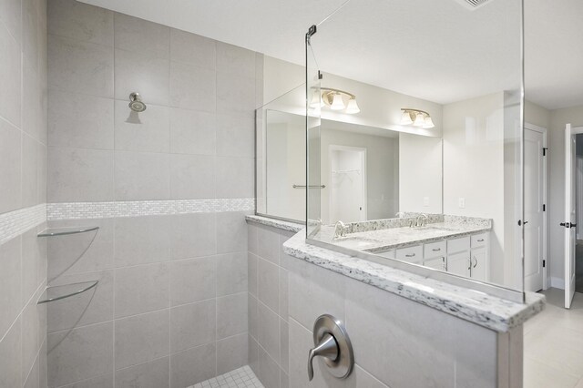 bathroom with tiled shower, vanity, tile patterned flooring, and tile walls