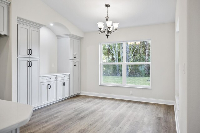 unfurnished dining area with an inviting chandelier and light wood-type flooring