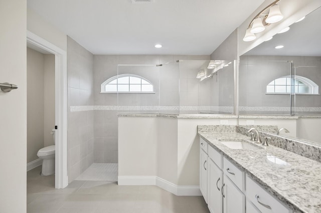 bathroom featuring toilet, a tile shower, vanity, and tile patterned floors