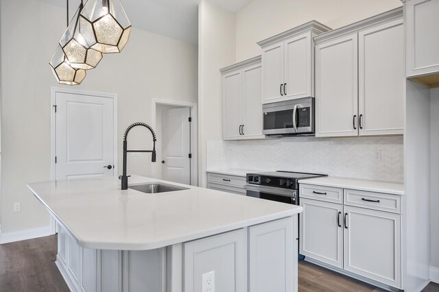 kitchen featuring dark wood-type flooring, a center island with sink, sink, hanging light fixtures, and stainless steel appliances