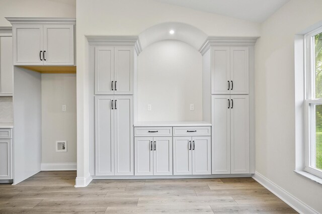 kitchen featuring a wealth of natural light, white cabinets, vaulted ceiling, and light wood-type flooring