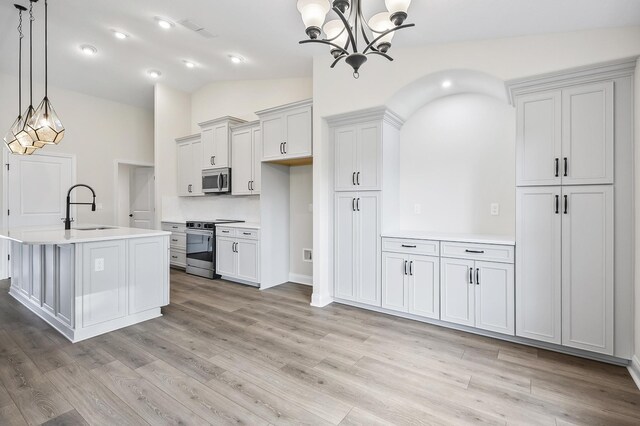 kitchen featuring stainless steel appliances, vaulted ceiling, a kitchen island with sink, sink, and decorative light fixtures