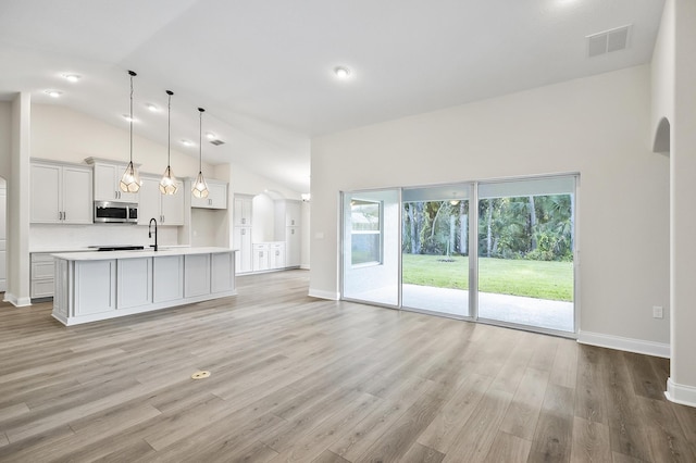 kitchen with a kitchen island with sink, sink, decorative light fixtures, high vaulted ceiling, and light hardwood / wood-style floors