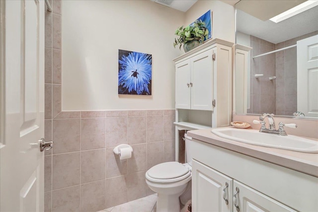 bathroom featuring vanity, toilet, tiled shower, and tile walls