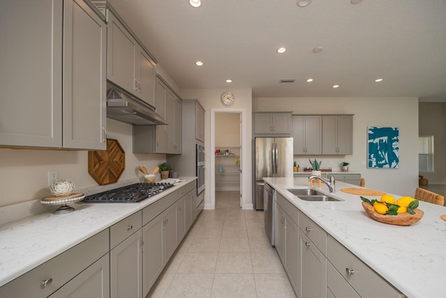 kitchen featuring gray cabinetry, exhaust hood, sink, appliances with stainless steel finishes, and light stone counters