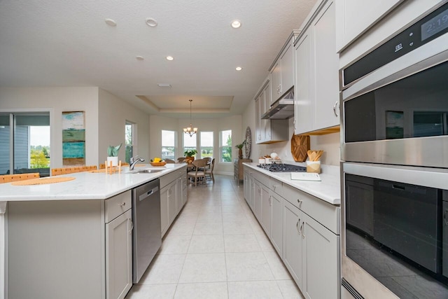 kitchen featuring gray cabinets, a kitchen island with sink, appliances with stainless steel finishes, and an inviting chandelier