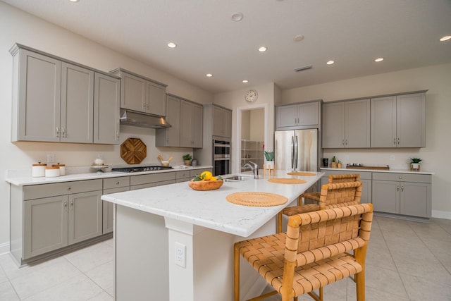 kitchen featuring gray cabinetry, sink, an island with sink, a breakfast bar area, and appliances with stainless steel finishes