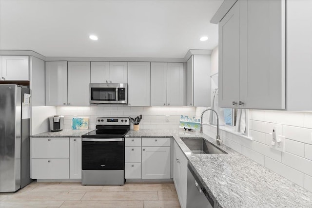 kitchen featuring light stone counters, tasteful backsplash, appliances with stainless steel finishes, and a sink