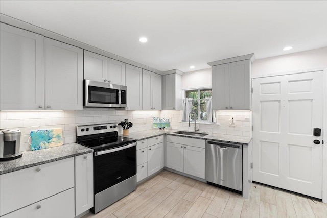 kitchen with a sink, light wood-style floors, backsplash, and appliances with stainless steel finishes