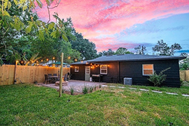 back house at dusk with a yard, a patio, and central air condition unit