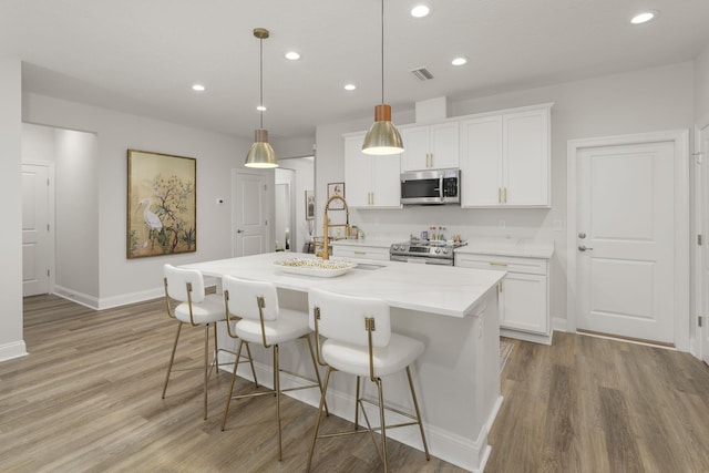 kitchen featuring white cabinets, appliances with stainless steel finishes, hanging light fixtures, and an island with sink