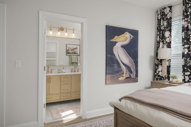 bedroom with ensuite bathroom, light hardwood / wood-style floors, and sink