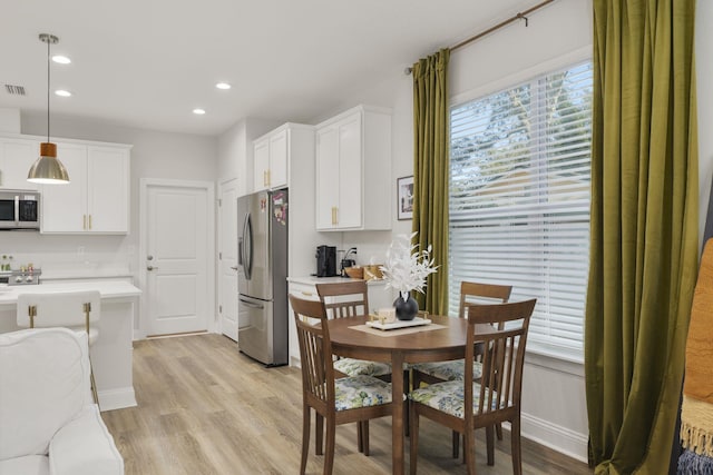 kitchen featuring stainless steel appliances, white cabinets, hanging light fixtures, and light hardwood / wood-style floors