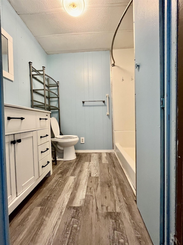 bathroom with vanity, a shower, wooden walls, hardwood / wood-style flooring, and toilet