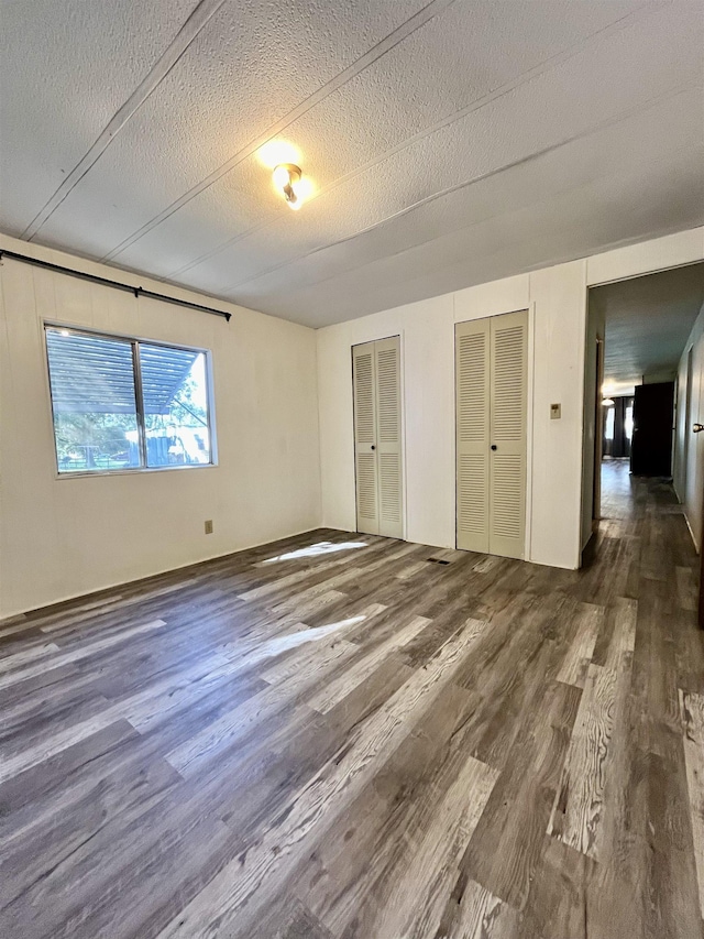 unfurnished bedroom featuring dark hardwood / wood-style flooring, a textured ceiling, and multiple closets