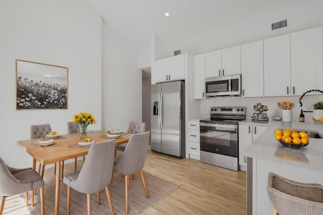 kitchen with white cabinets, sink, a towering ceiling, light hardwood / wood-style floors, and stainless steel appliances