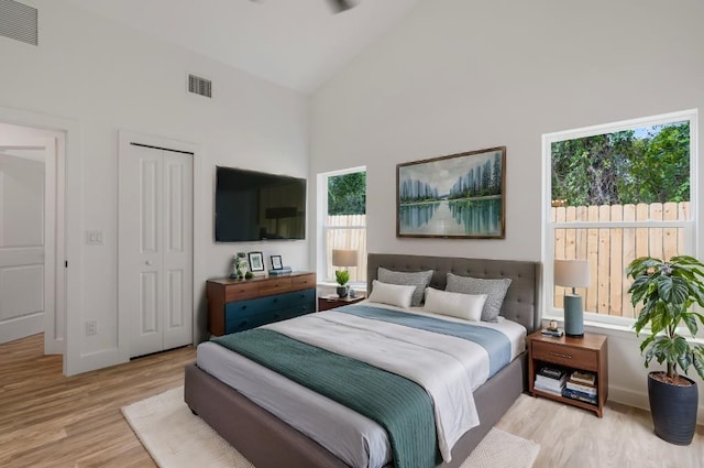 bedroom featuring light wood-type flooring, high vaulted ceiling, and a closet