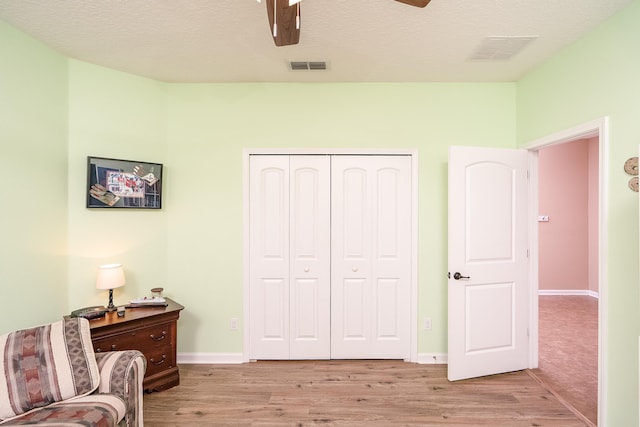 living area featuring a textured ceiling, light hardwood / wood-style flooring, and ceiling fan