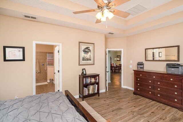 bedroom with ensuite bathroom, ceiling fan, light hardwood / wood-style floors, and a textured ceiling