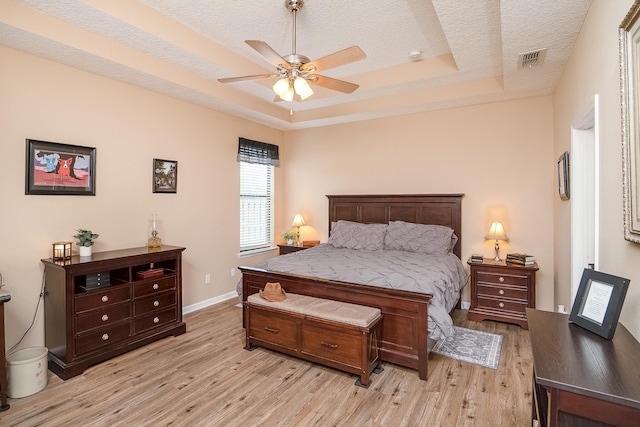 bedroom featuring a textured ceiling, light wood-type flooring, a tray ceiling, and ceiling fan