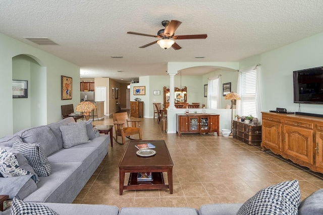 tiled living room with ceiling fan, ornate columns, and a textured ceiling