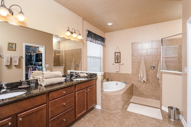 bathroom featuring plus walk in shower, vanity, a textured ceiling, and tile patterned floors