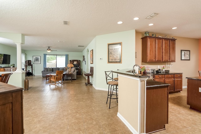 kitchen with kitchen peninsula, ornate columns, a breakfast bar, a textured ceiling, and ceiling fan