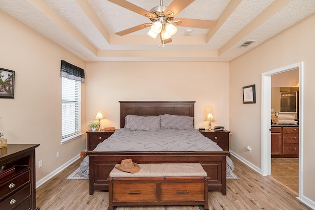 bedroom featuring a raised ceiling, ceiling fan, light hardwood / wood-style floors, and a textured ceiling