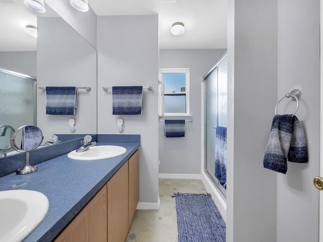 full bath with a shower stall, double vanity, and baseboards