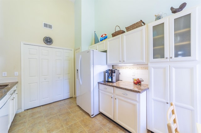 kitchen featuring tasteful backsplash, white fridge with ice dispenser, white cabinets, and dark stone counters