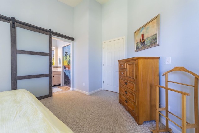 bedroom with light carpet, a towering ceiling, a barn door, and ensuite bathroom