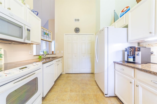 kitchen featuring white cabinetry, dark stone countertops, decorative backsplash, light tile patterned floors, and white appliances