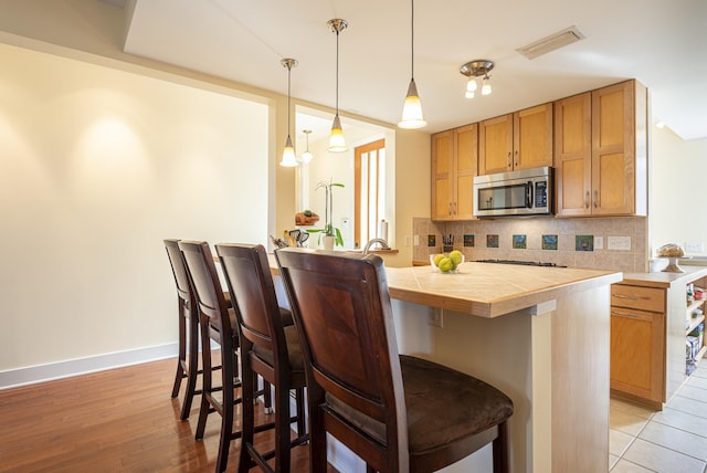 kitchen featuring decorative light fixtures, a kitchen breakfast bar, decorative backsplash, kitchen peninsula, and light hardwood / wood-style flooring