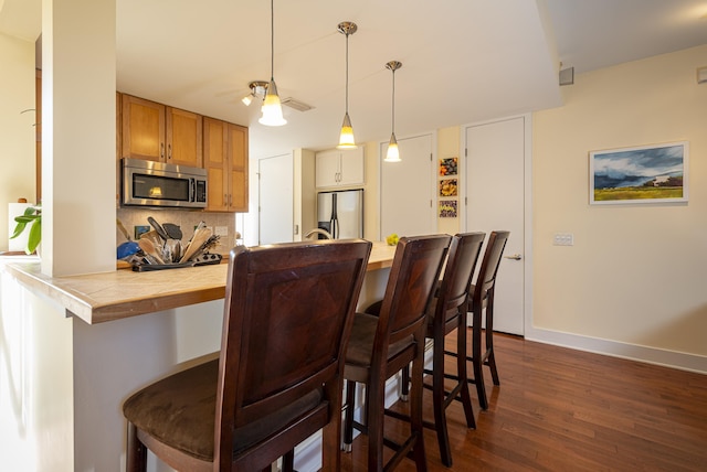 kitchen with a kitchen bar, dark hardwood / wood-style flooring, kitchen peninsula, stainless steel appliances, and decorative backsplash