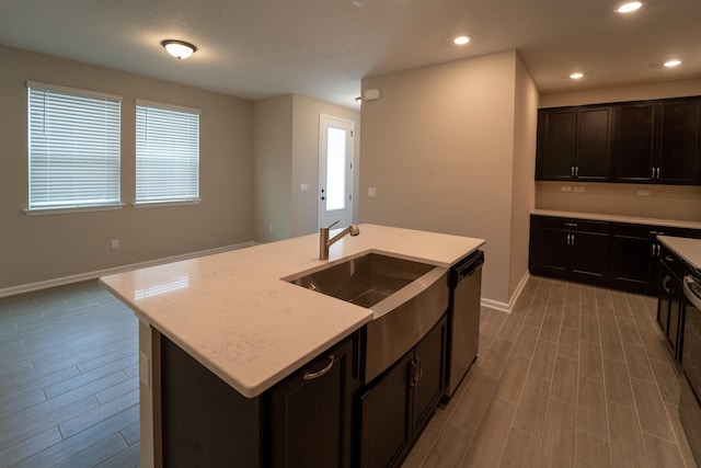 kitchen with stainless steel dishwasher, sink, a kitchen island with sink, and hardwood / wood-style flooring