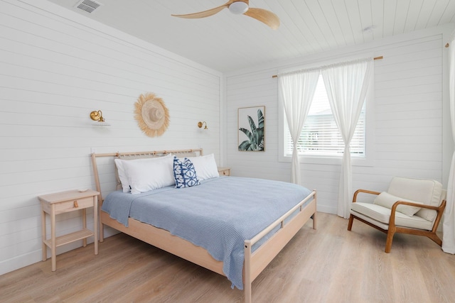 bedroom with light hardwood / wood-style floors, ceiling fan, and wood walls