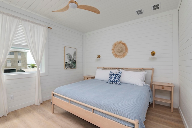 bedroom with ceiling fan, wood walls, and light hardwood / wood-style flooring