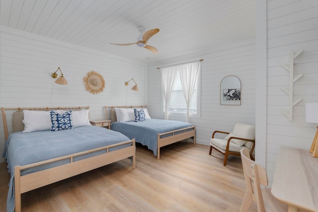 bedroom featuring ceiling fan, wood walls, and light wood-type flooring