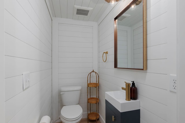 bathroom with vanity, toilet, and wood walls