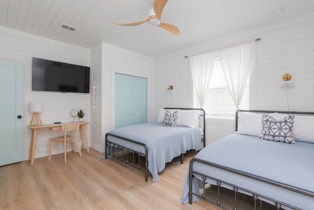 bedroom with light wood-type flooring, a closet, ceiling fan, and wooden walls