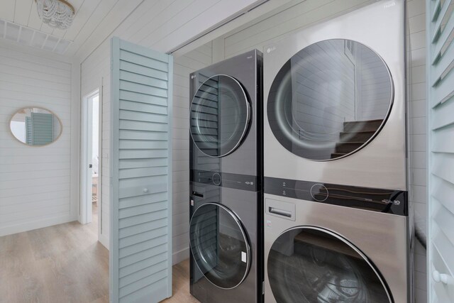 washroom featuring wooden walls, stacked washing maching and dryer, and light hardwood / wood-style floors